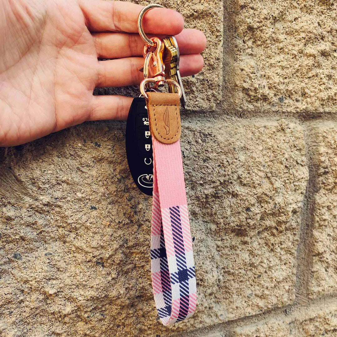 People holding pink cream black multicolor plaid hand wrist lanyard with keys on the hand